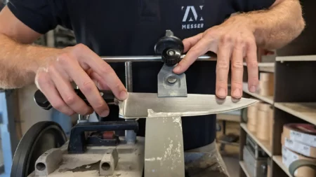 Professioneller Schleifservice und Lohnschleifen einer hochwertigen Messerklinge auf einer wassergekühlten Schleifmaschine in der Manufaktur von ZM-Messer in Haag am Hausruck, Oberösterreich.