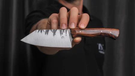 Handgeschmiedetes Ko-Bunka Allzweckmesser aus Carbonstahl mit sichtbarer Hammerschlag-Optik und edlem Wüsteneisenholz-Griff, gehalten von Messerschmied, gefertigt in Haag am Hausruck, Oberösterreich